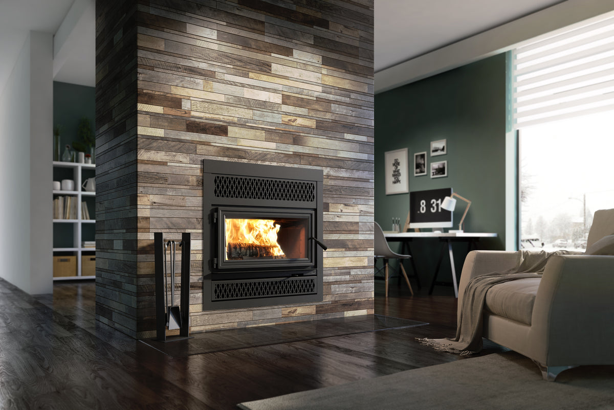 A modern wood-look fireplace insert with a black metal frame and an active fire, set within a tall stone veneer wall in a contemporary living room with dark wood floors, a beige armchair, and a green accent wall.