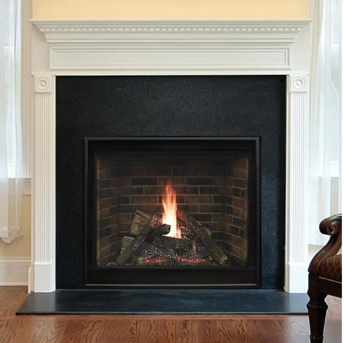 A gas fireplace insert with a black surround and glass front, showing a realistic brick firebox with logs and flames, set within a white fireplace mantel.
