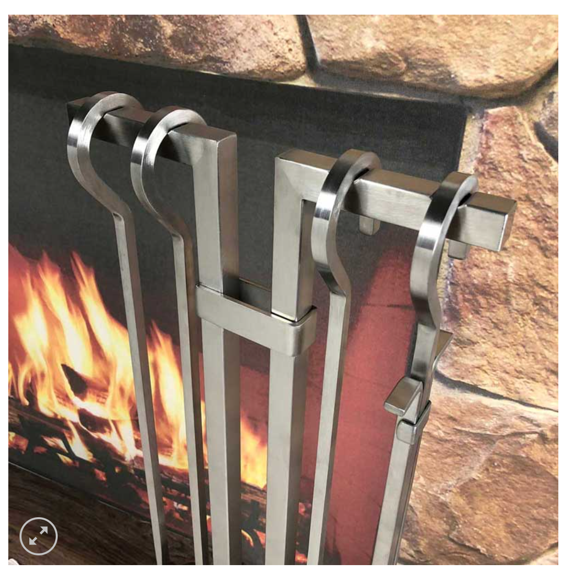 Close up of the brushed stainless steel tool set in front of a fire in a fireplace