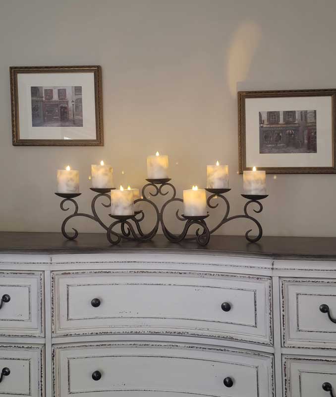 Decorative candle holder with lit candles on a dresser against a wall with framed pictures.