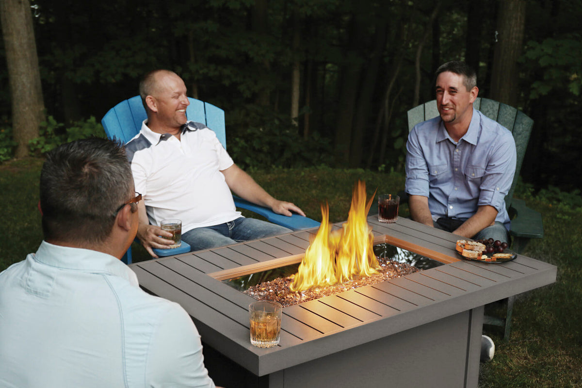 Three men sitting around a fire pit table in a backyard setting.