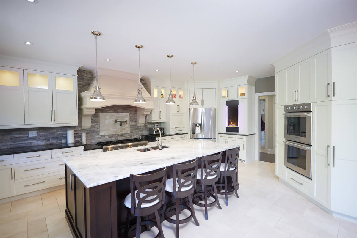 A modern kitchen island with a white marble-look countertop and dark wood base, surrounded by four dark wood bar stools. The kitchen features white cabinets, stainless steel appliances, a stone backsplash, and pendant lights.