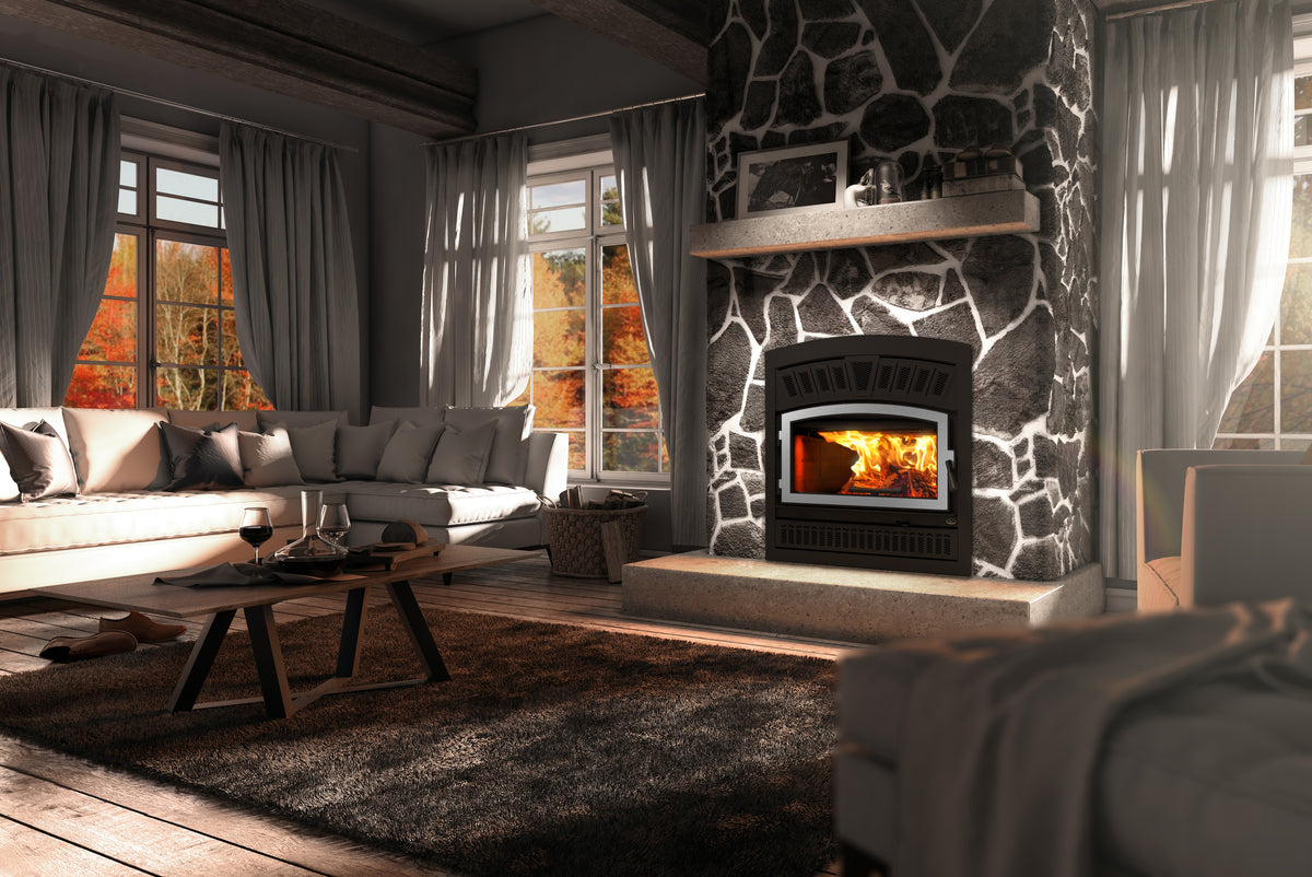 A modern black wood-burning fireplace with a glowing fire, set into a dark stone wall in a cozy, rustic living room with a sectional sofa, wooden coffee table, and large windows.