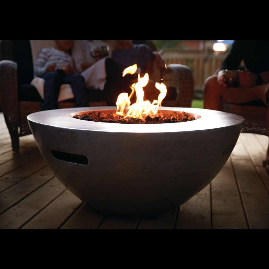 Fire pit with flames on a wooden deck, people sitting in the background