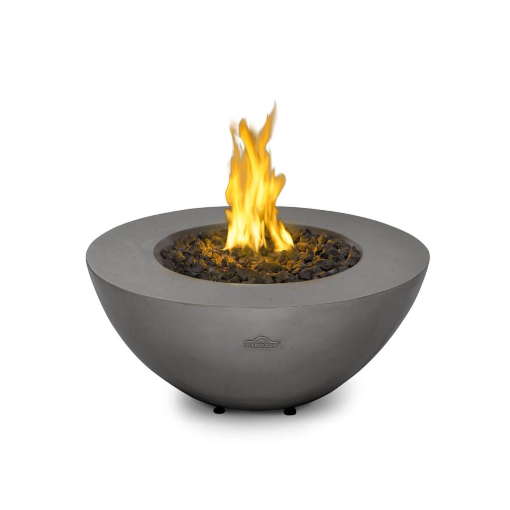 A modern concrete bowl fire pit with a glowing yellow and orange flame, filled with dark decorative stones, shown on a solid white background.