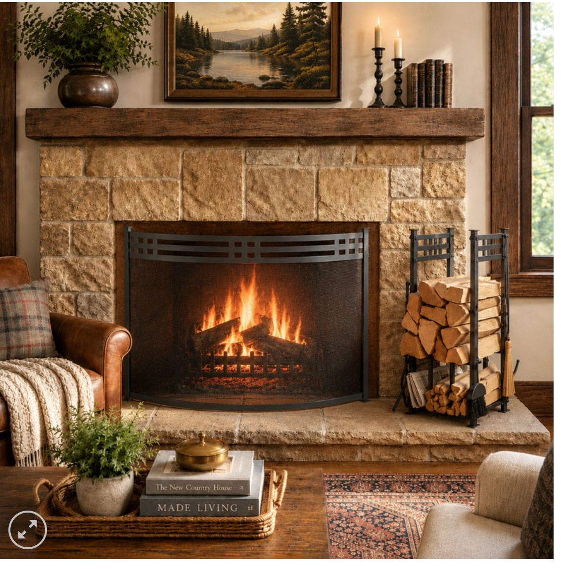 A cozy living room scene centered on a stone fireplace with a black metal fire screen, warm fire inside, stacked firewood on a rack, mantel decor, and part of an armchair and coffee table in the foreground.