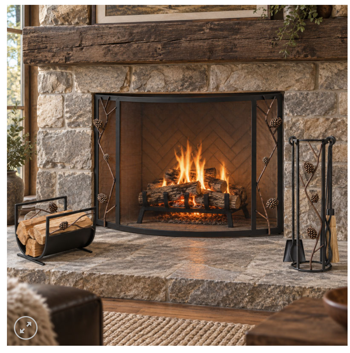 Pine cone fireplace screen in front of a burining fire in a stone fireplace with a wood mantel. The pine tool set and pine cone wood holder are also in this image