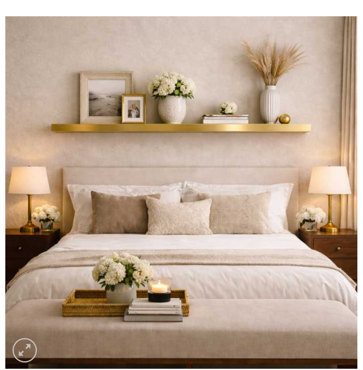 shelf on white wall in a bedroom shelf has a vase with flowers a picture frame and books. bed has vase with flowers, candle and books on stool at base of bed