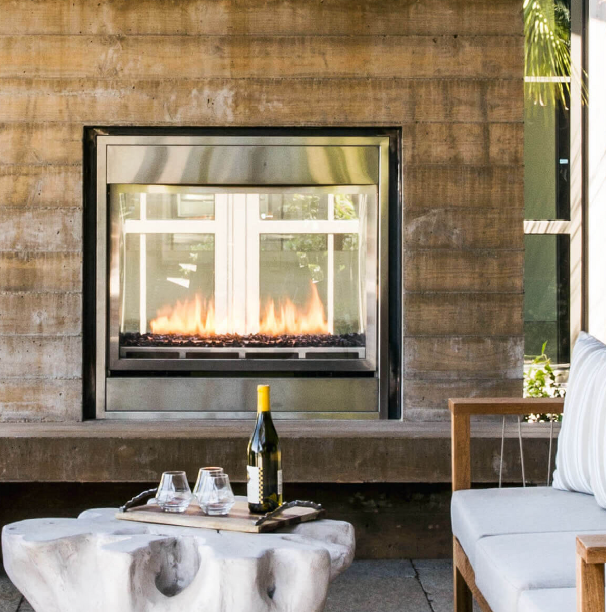 firplace built n to a stone structure with a bottle of wine and glasses on a table ear a sofa
