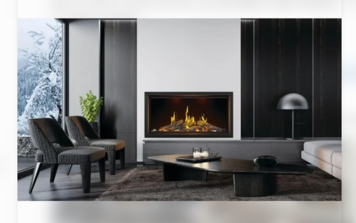A modern living room scene featuring a black-framed gas fireplace with glowing yellow and orange flames, set against a white wall with dark wood paneling. Two dark upholstered armchairs, a low black coffee table, and a light gray sofa are arranged in the room.