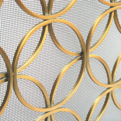 Close-up of a decorative gold metal screen with interlocking circular rings over a white mesh background.