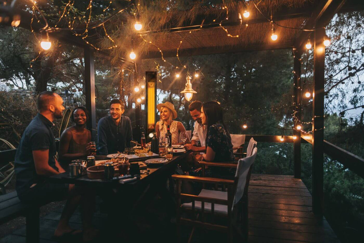 Group of people sitting around a table on a wooden deck with string lights