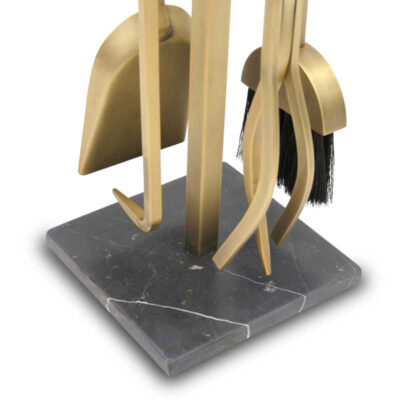Set of gold fireplace tools on a dark marble stand with a white background