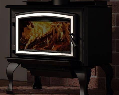 A black wood-burning stove with a glass door showing a glowing fire inside, set against a dark background with a brick wall.