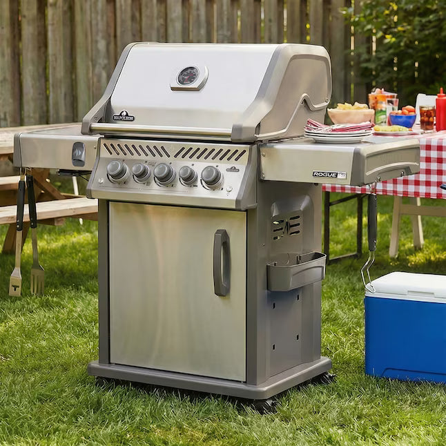 Grill outside in a backyard ready to grill food and a blue cooler is on the grass