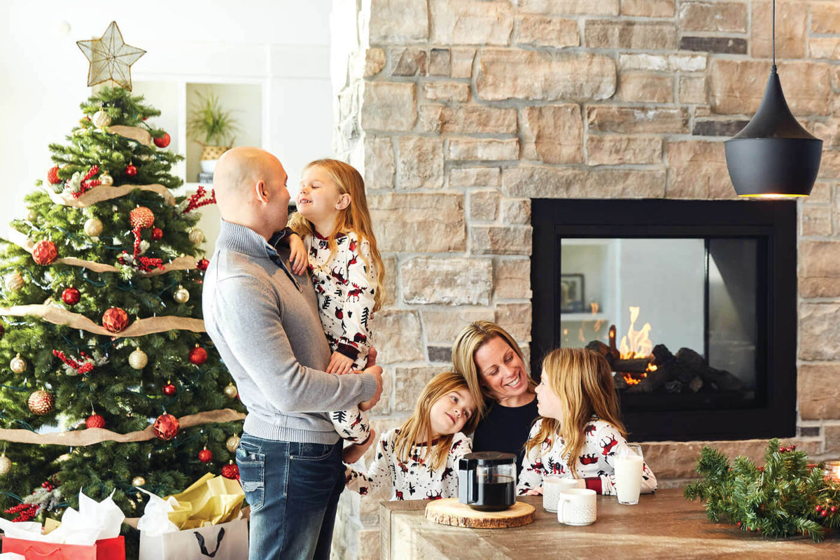Family gathered around a fireplace with a decorated Christmas tree in the background.