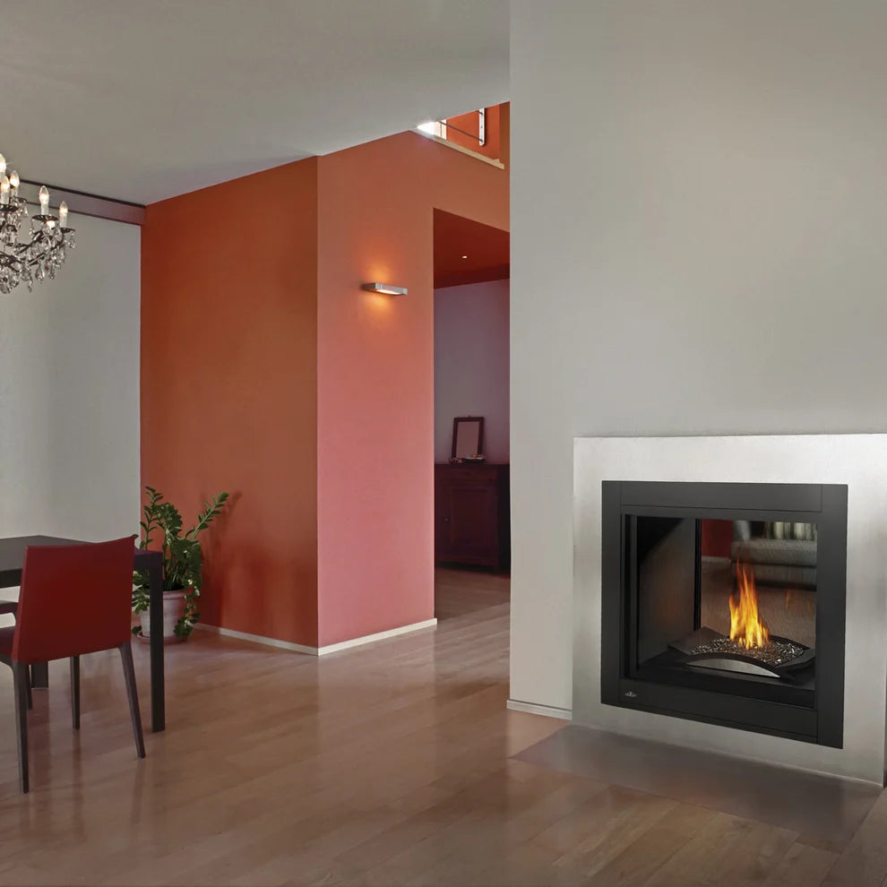 A modern gas fireplace insert with a black frame and active fire, set into a white wall in a contemporary living space with light wood floors and an orange accent wall.