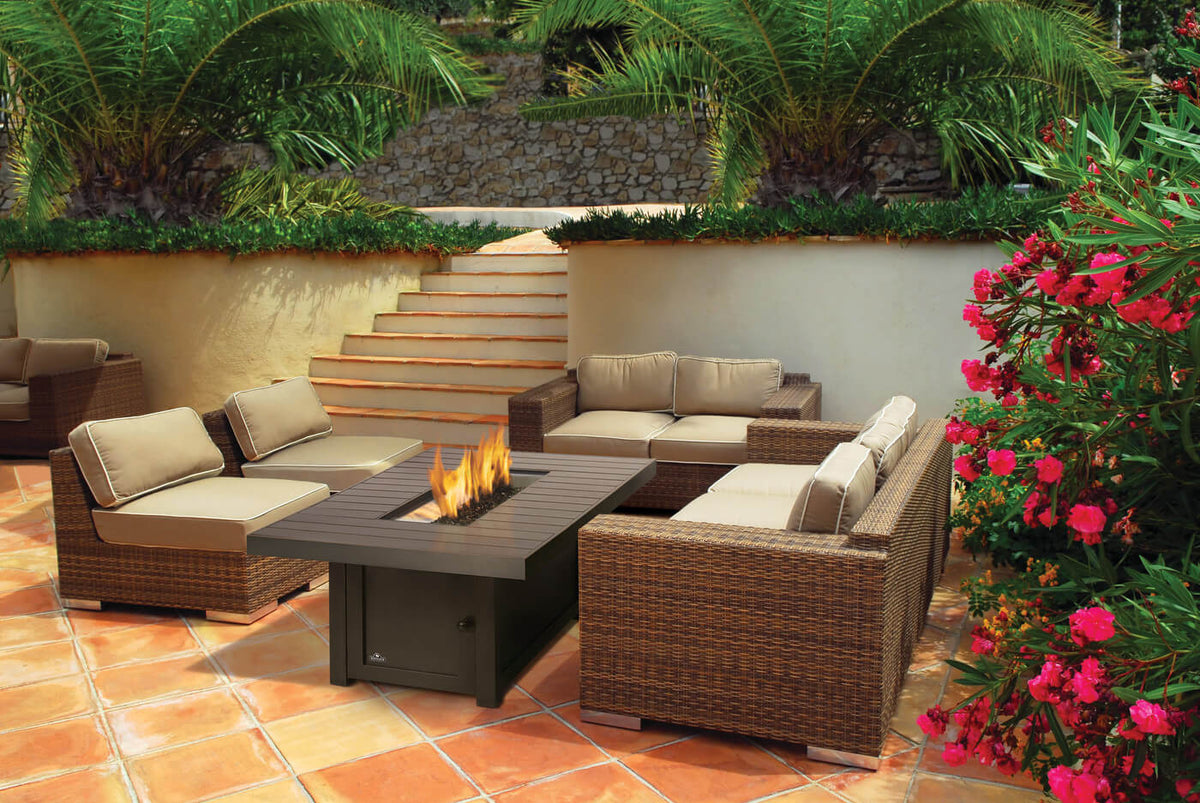 Outdoor patio with wicker furniture and fire pit surrounded by plants and flowers.