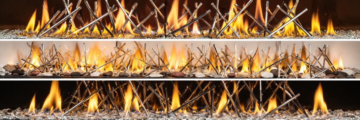 A close-up view of a decorative fireplace or stove insert with multiple horizontal rows of thin metallic spikes and bright yellow-orange flames rising above, set against a dark background with gray and metallic gravel at the base.